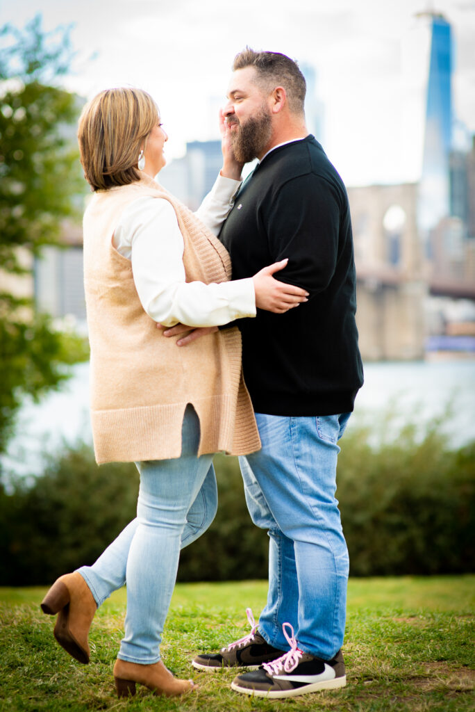 At Brooklyn Bridge Park a Couple stand together in an embrace looking endearingly at each other. Captured by Corey Lamar Photography