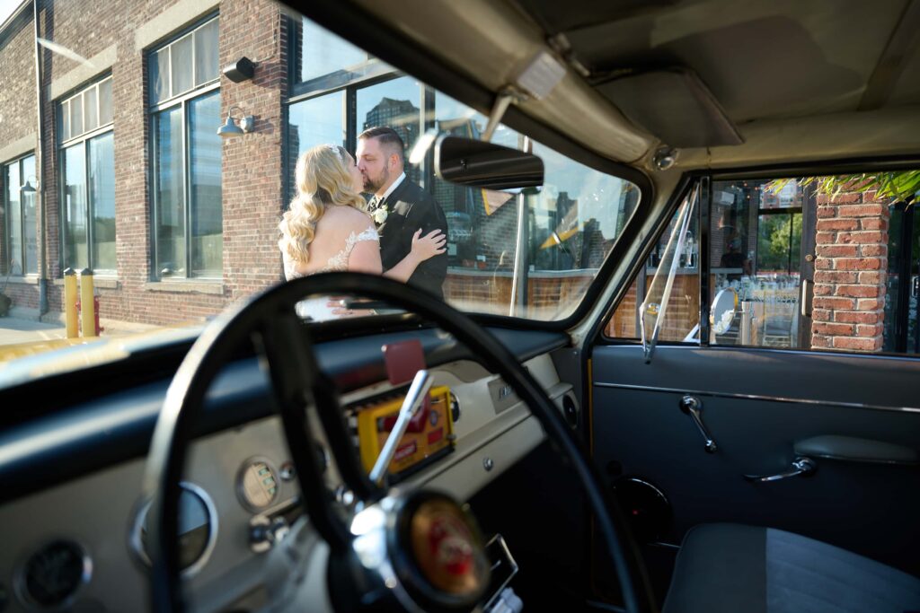 Looking through the driving glass of the Checkered Cab, bride and groom kiss outside the Wedding Venue, Battello