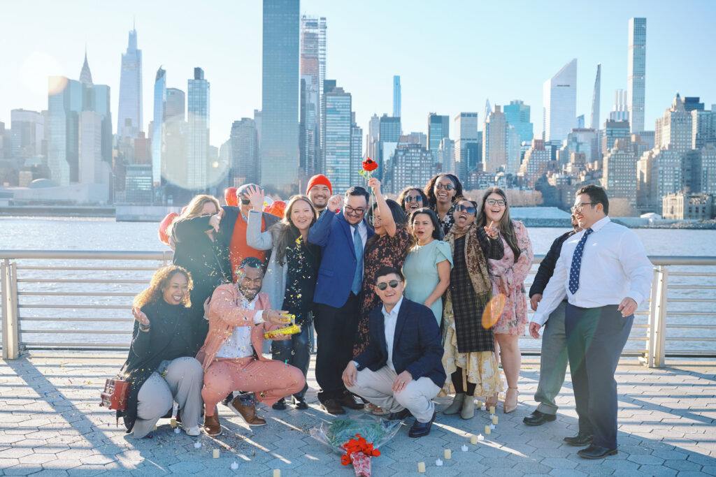 Friends Gather together in front of the New York City Skyline, after a successful Proposal.  Confetti Fires off catching some off guard, everyone laughs