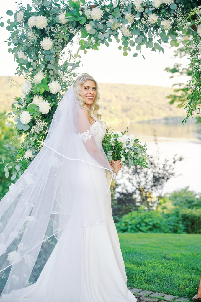 Bride stands holding her flows in front of her floral arch after her Wedding Ceremony at the Clements Castle in Connecticut, photo captured by Nyc wedding Photographer Corey Lamar Photography