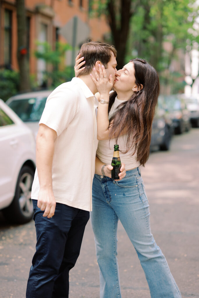 Vanessa kissing Mark while holding champagne during a West Village engagement session