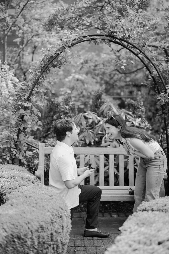 Black and white West Village engagement photo of Mark proposing to Vanessa under a garden arch