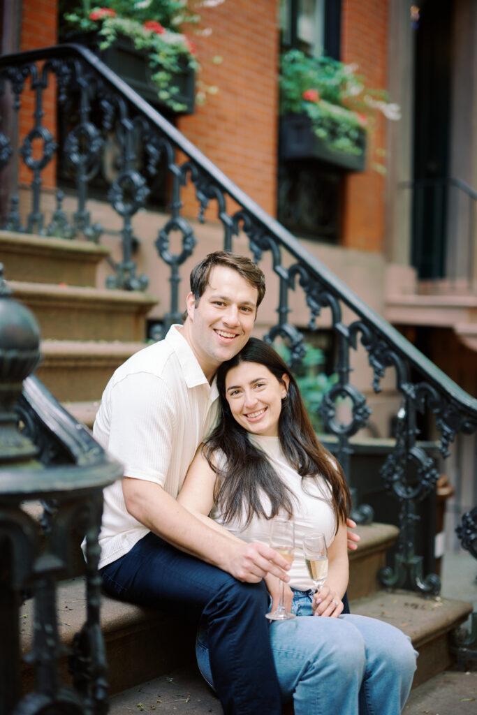 Mark and Vanessa toasting with champagne flutes on a West Village brownstone stoop